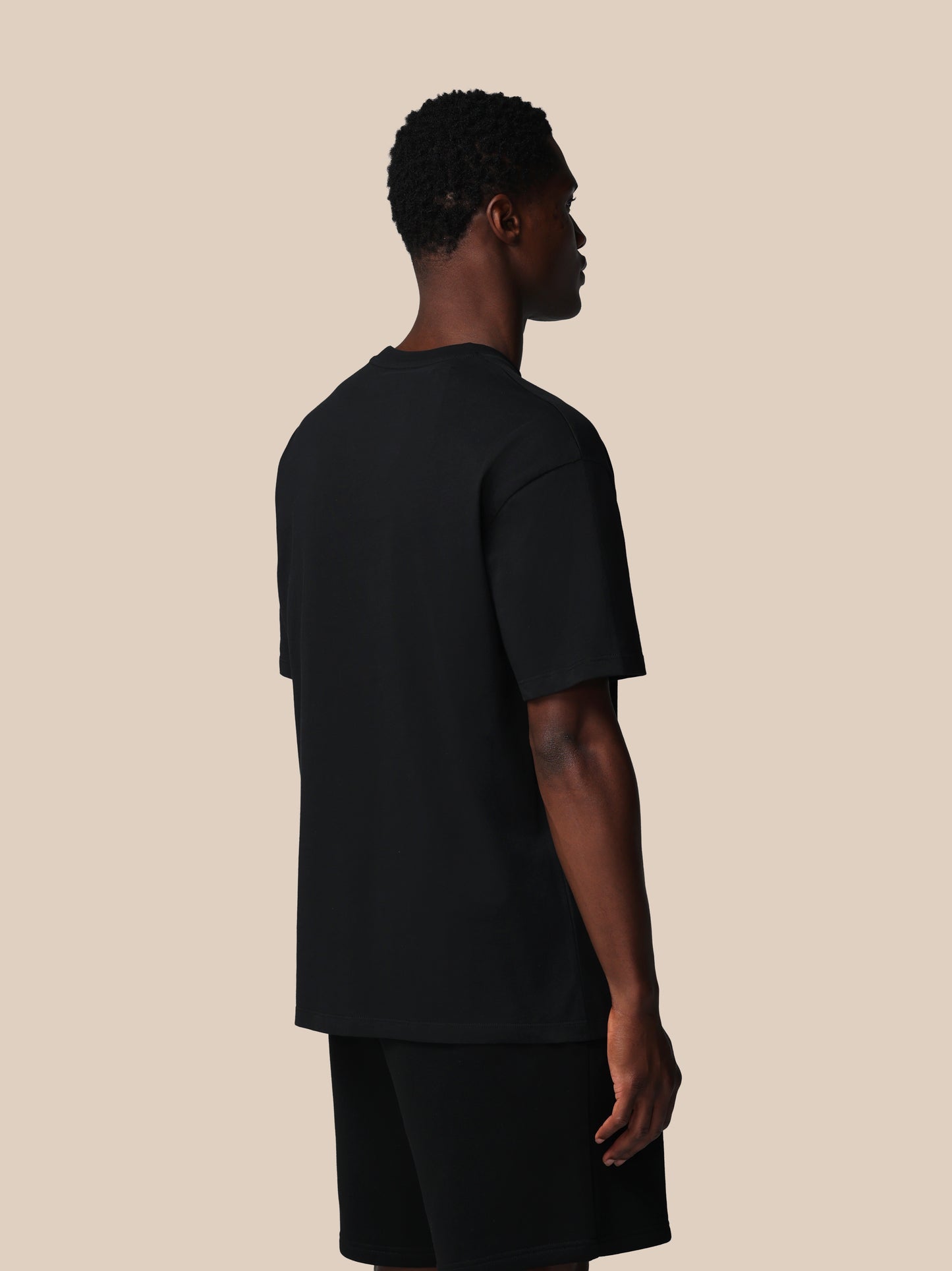 Person wearing a black t-shirt and shorts on a beige background
