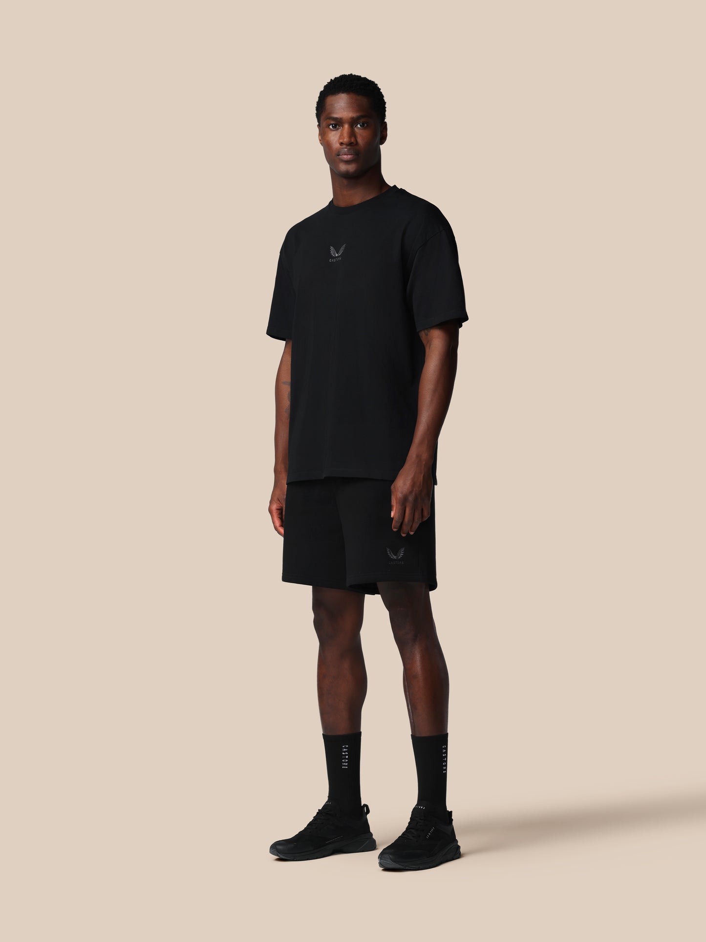 Man wearing a black t-shirt, shorts, and socks on a beige background
