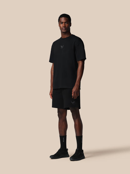 Man wearing a black t-shirt, shorts, and socks on a beige background