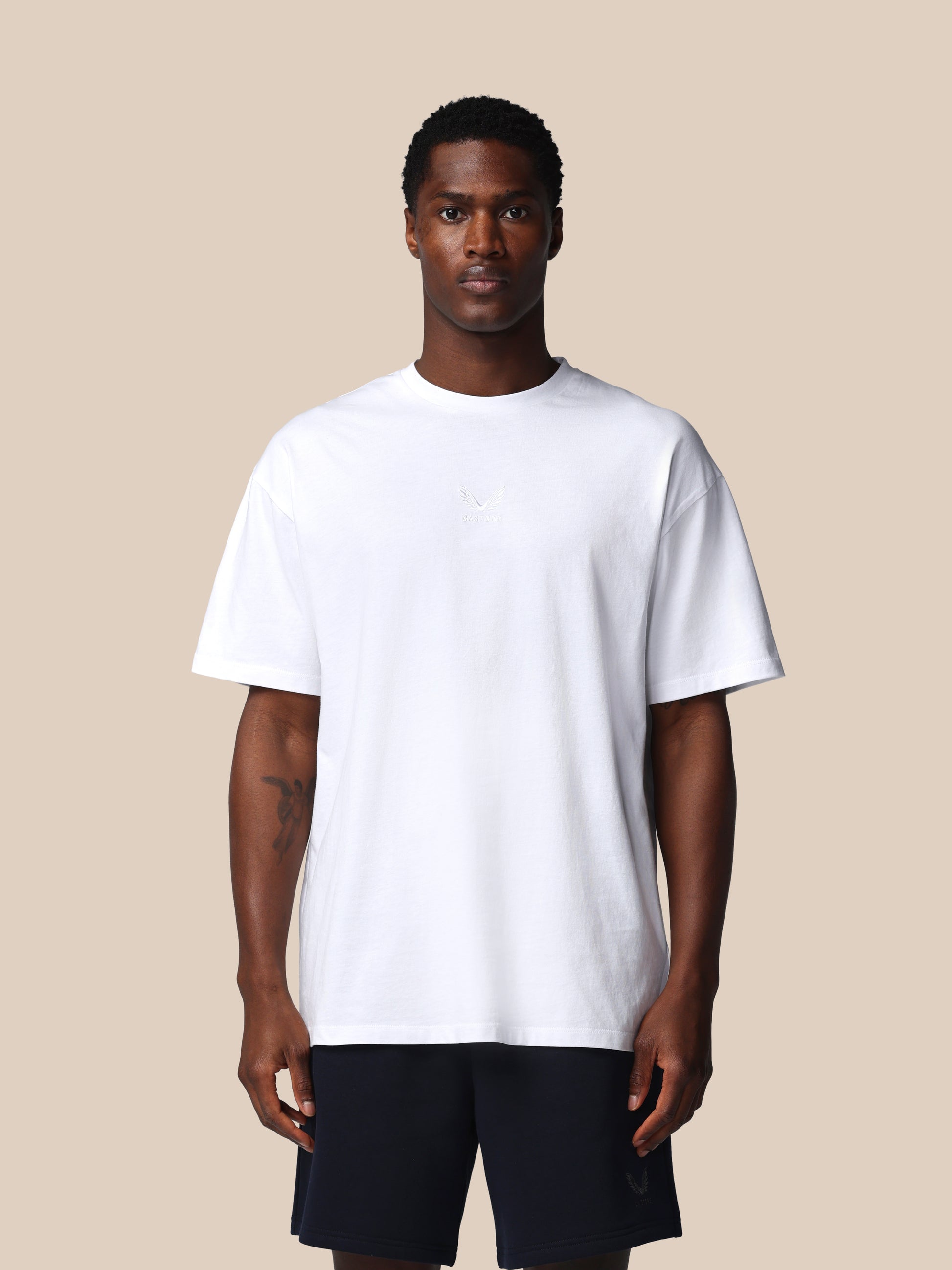 Man wearing a plain white t-shirt and black shorts on a beige background