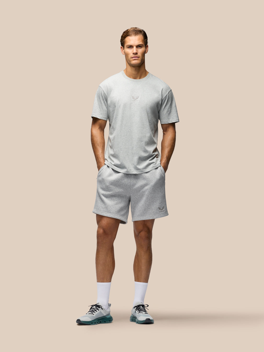 A man modeling a light gray short-sleeve t-shirt and matching light gray shorts against a solid beige background.