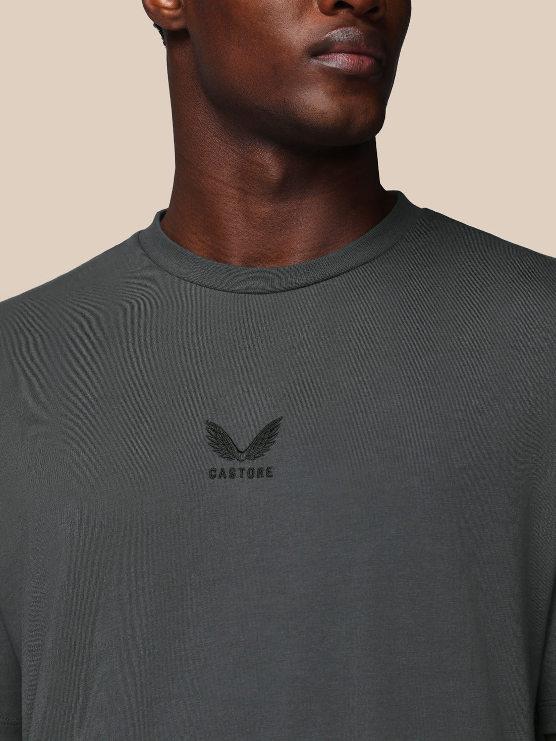 Person wearing a dark gray t-shirt with a logo on a beige background