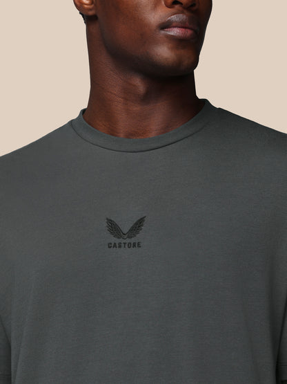 Person wearing a dark gray t-shirt with a logo on a beige background