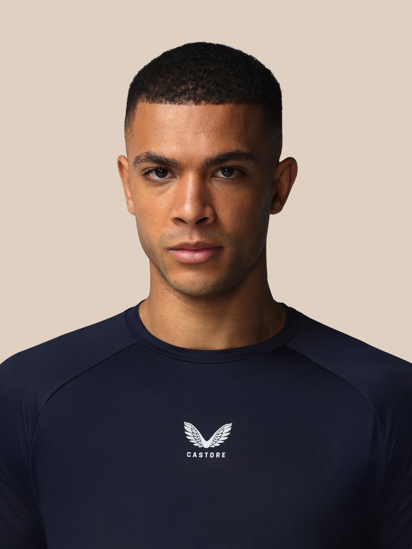 Man wearing a navy blue shirt with a logo on a beige background