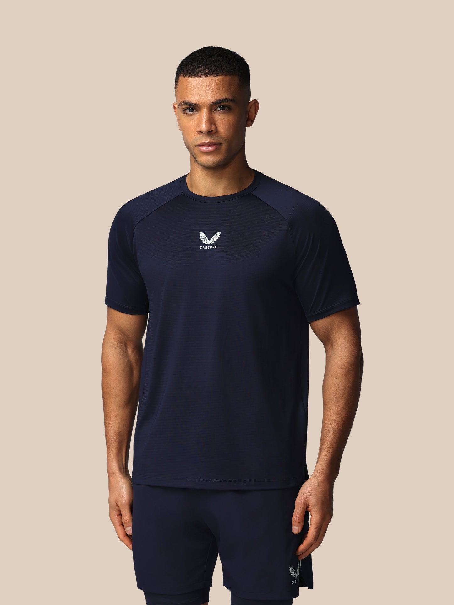 Man wearing a navy athletic outfit with a logo on a beige background