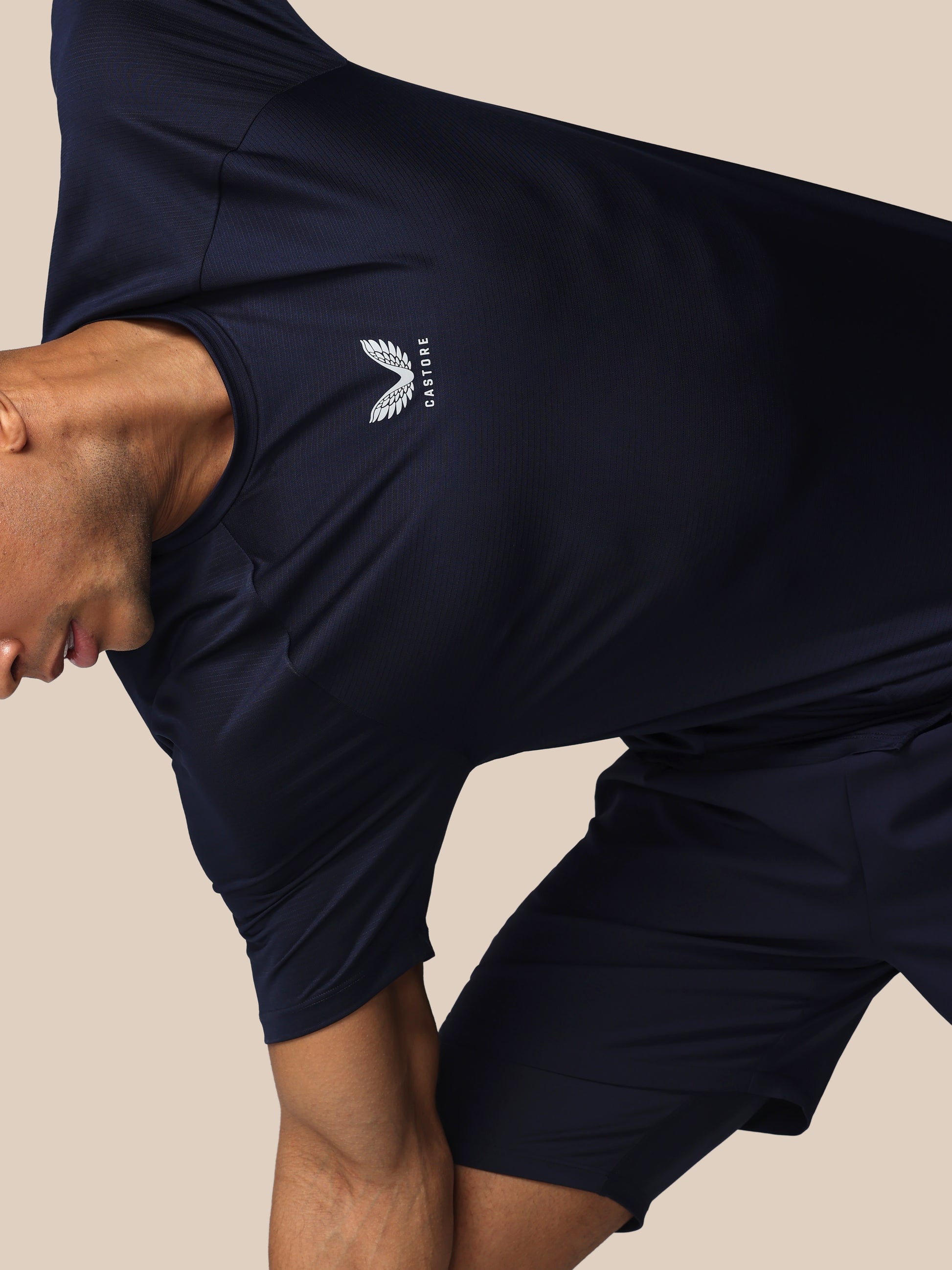Person wearing navy athletic shorts with a logo on a beige background