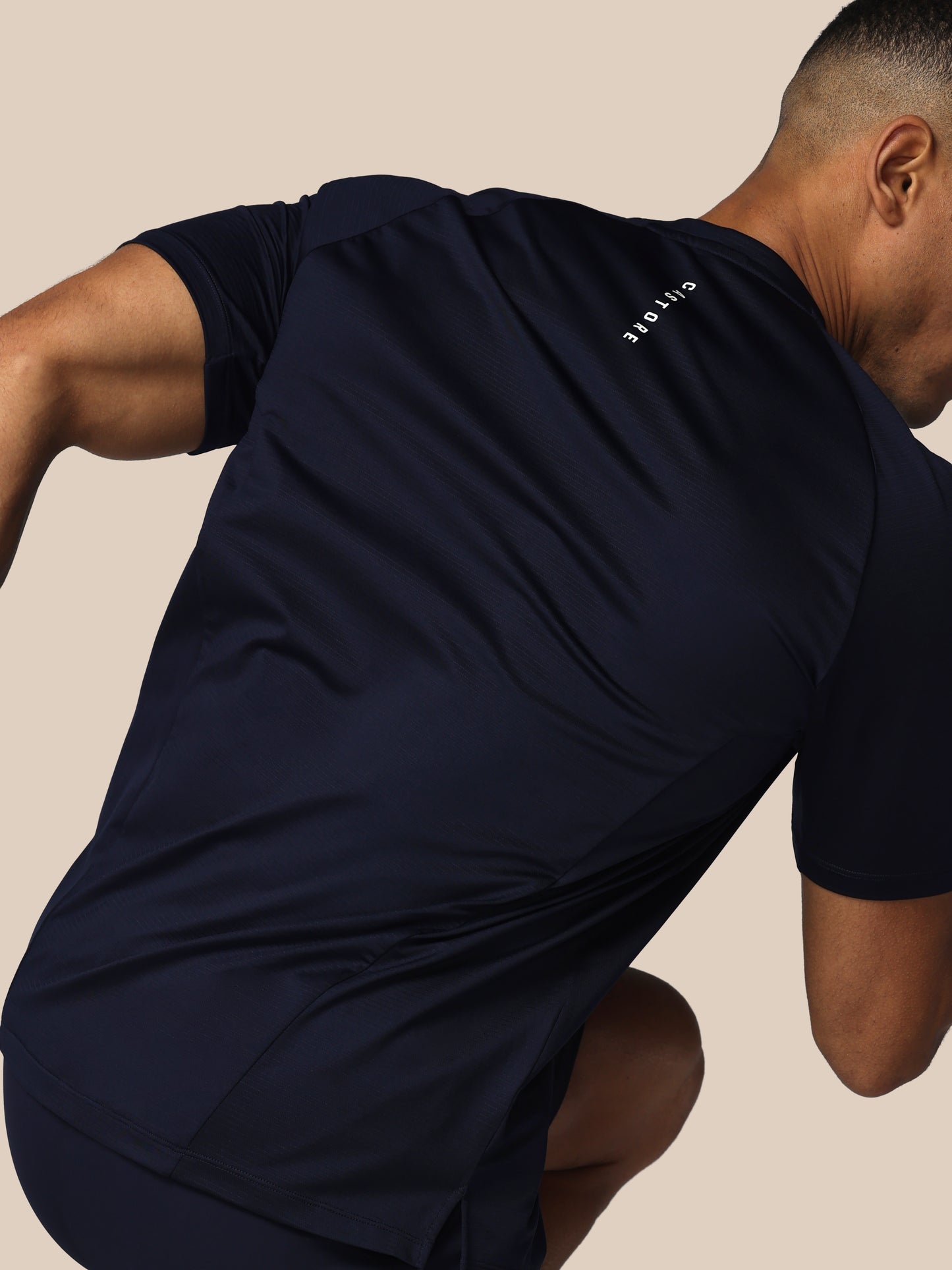 Man wearing a navy blue athletic outfit with a visible brand logo on a beige background