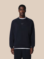 Man wearing a black sweatshirt with a logo on a beige background