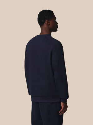 Person wearing a navy blue sweatshirt and pants on a beige background