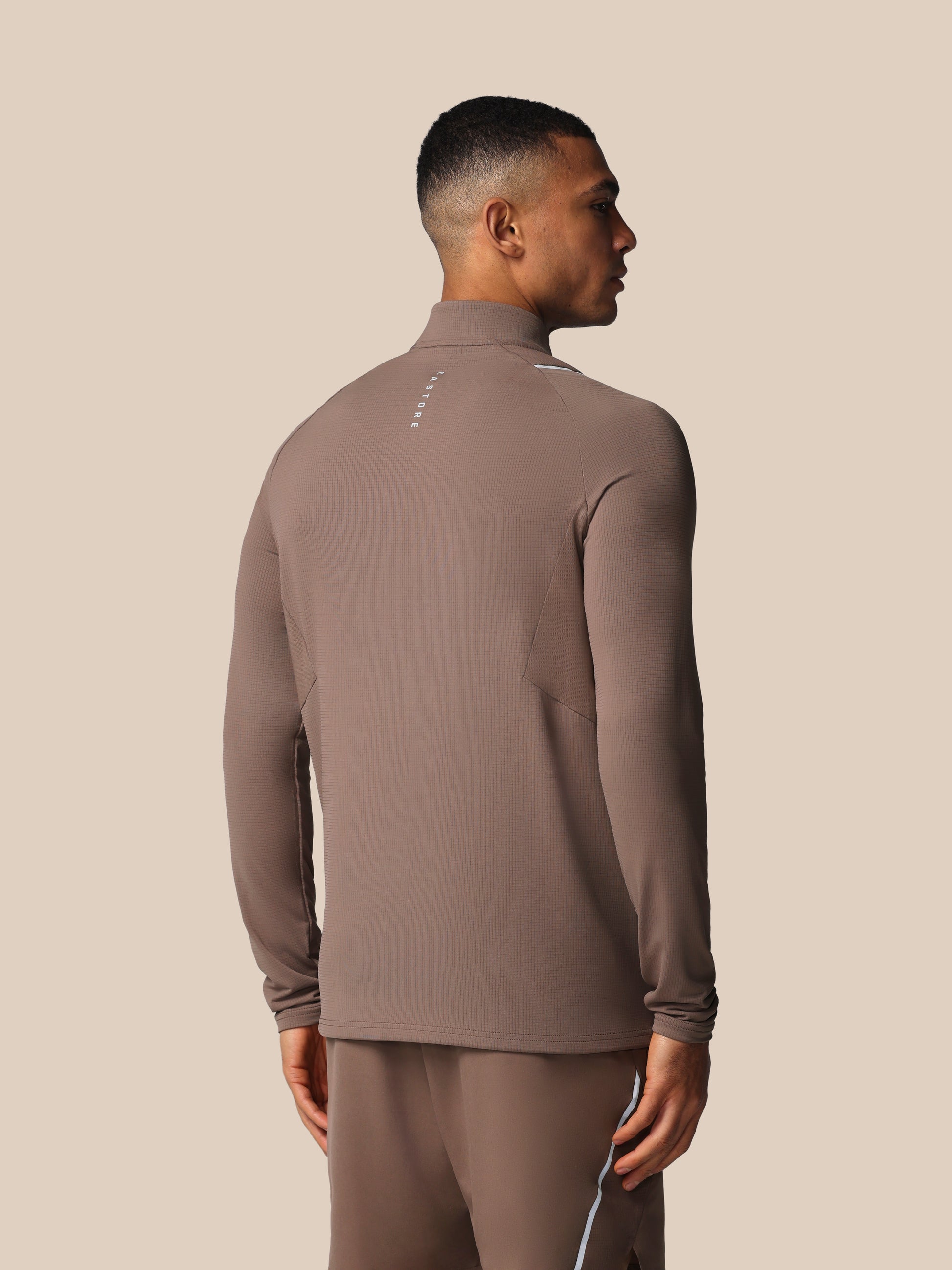 Man wearing a brown turtleneck and pants against a beige background