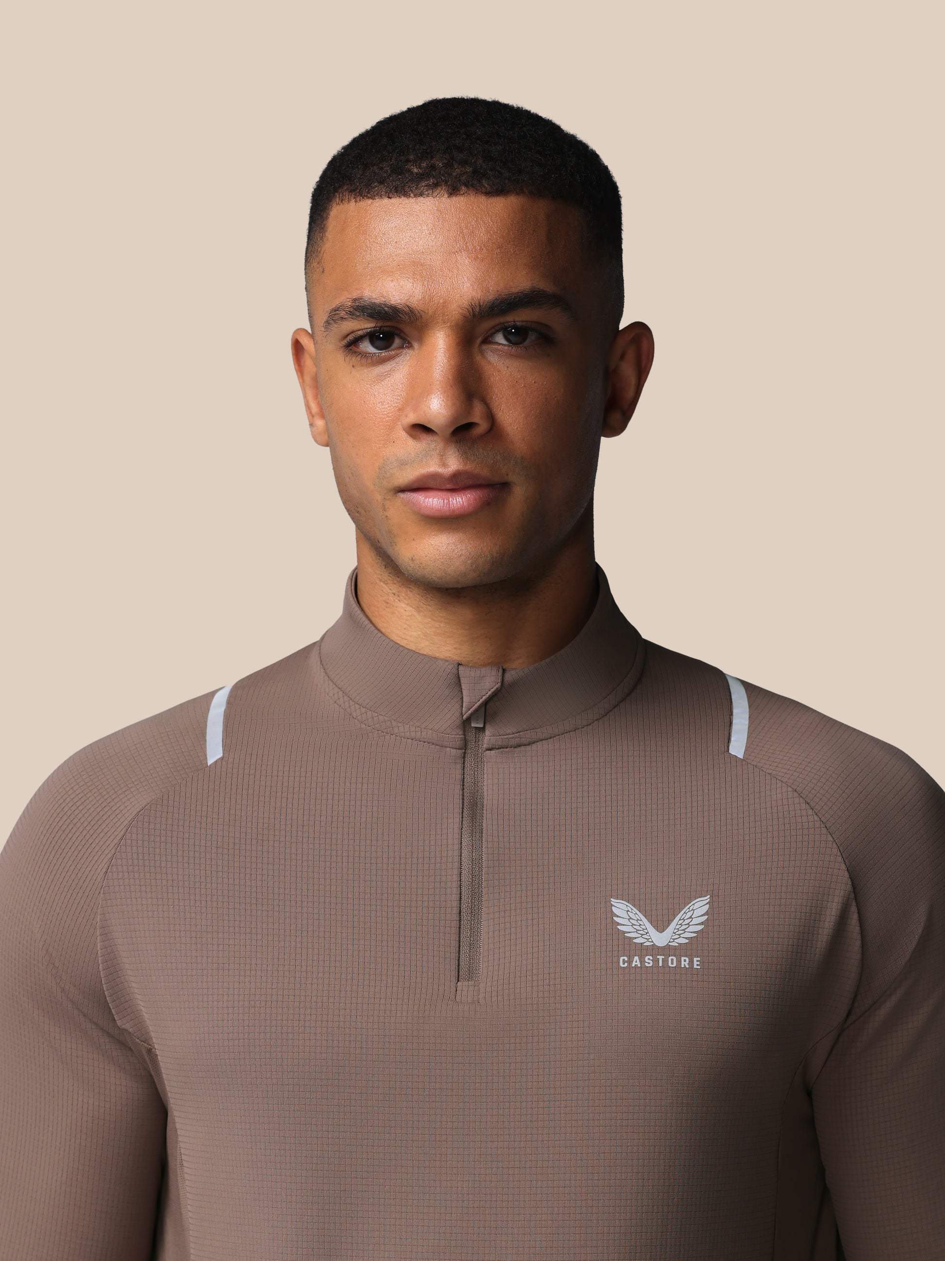 Man wearing a brown athletic jacket with a logo on a beige background