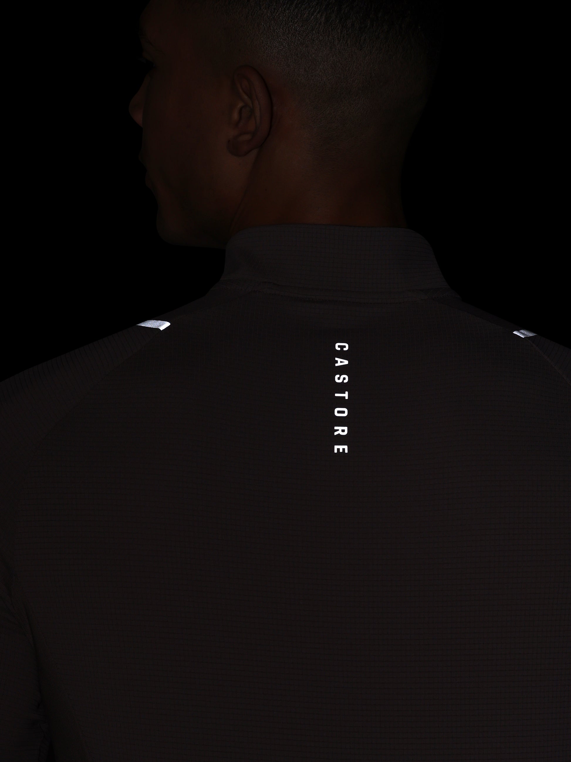Person wearing a dark shirt with 'Castore' branding on the back against a black background