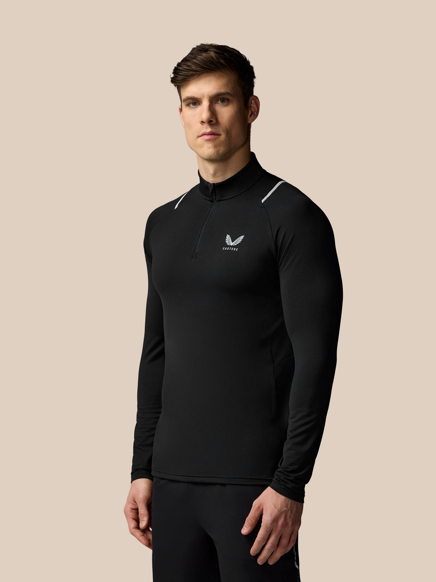 Man wearing a black long-sleeve athletic shirt with a logo on a beige background