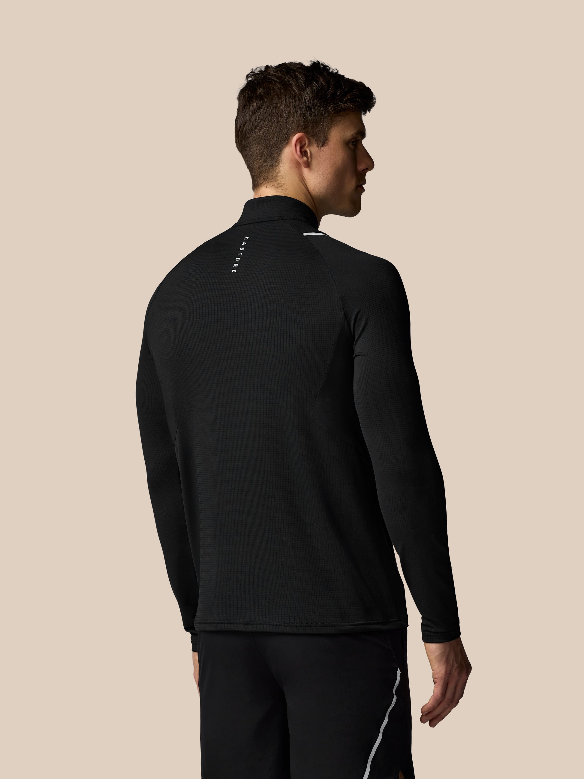 Man wearing a black athletic jacket and pants on a beige background