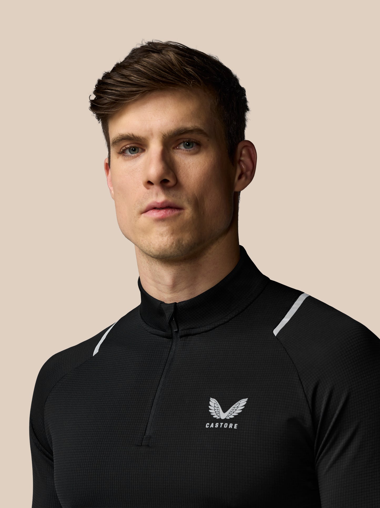 Man wearing a black athletic jacket with a logo on a beige background