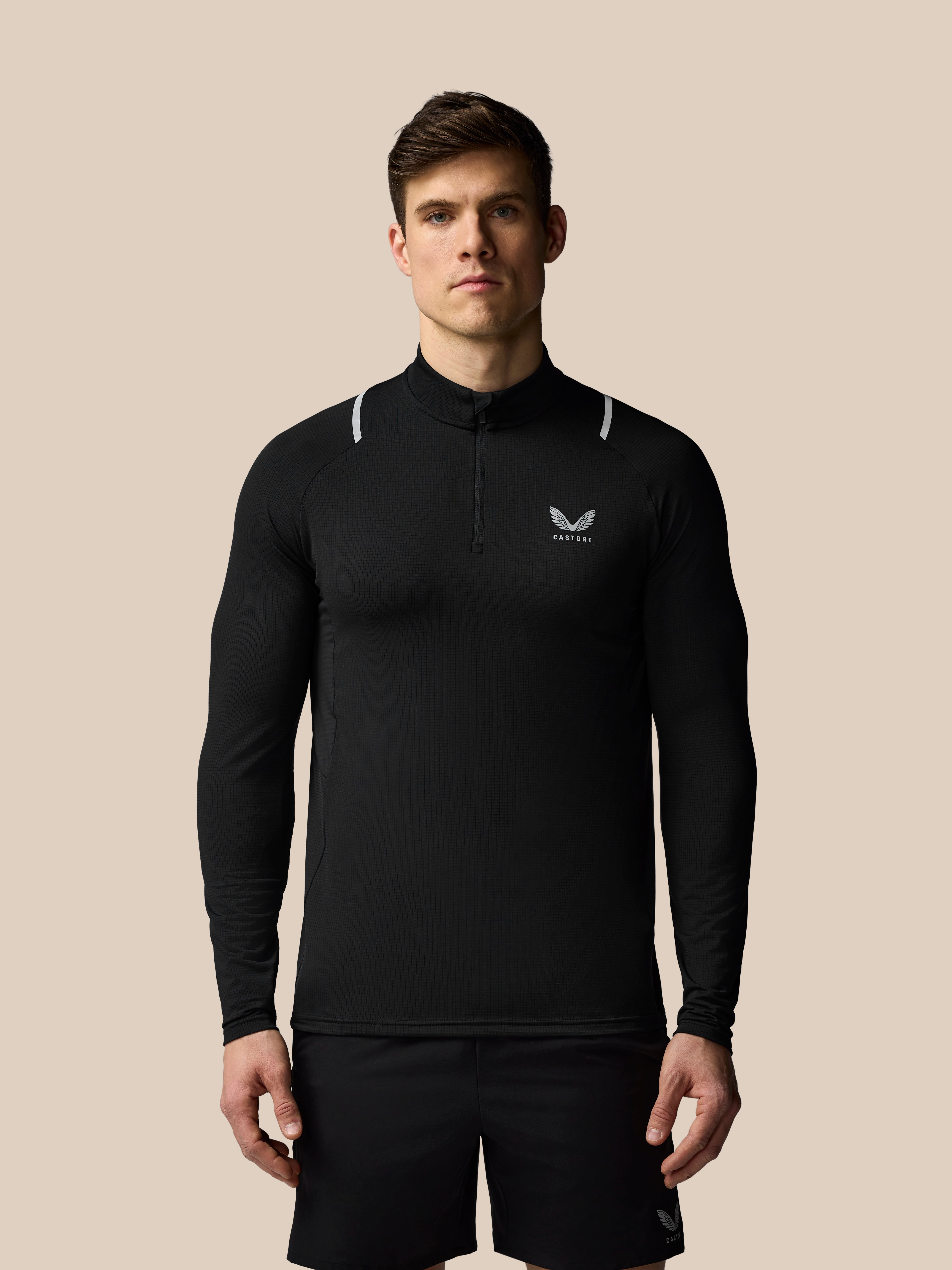 Man wearing a black long-sleeve athletic shirt with a logo on a beige background