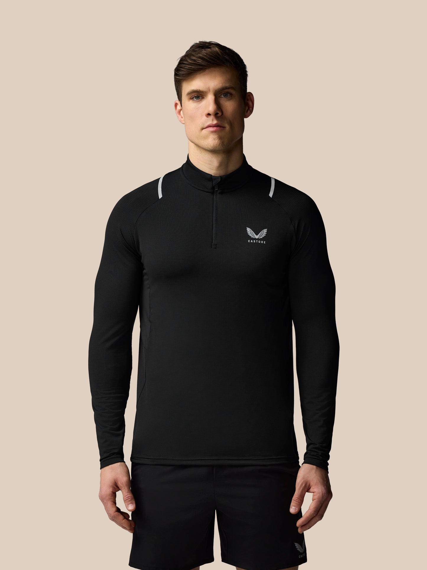 Man wearing a black long-sleeve athletic shirt with a logo on a beige background