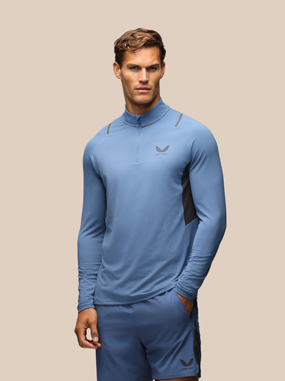 A male model wearing a light blue athletic quarter-zip pullover and matching shorts with dark gray side panels and logos, set against a solid beige background.