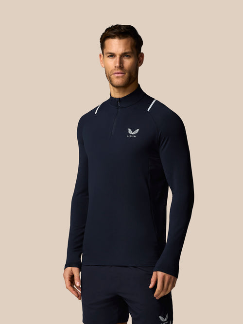 Man wearing a navy long-sleeve athletic shirt with a logo on a beige background