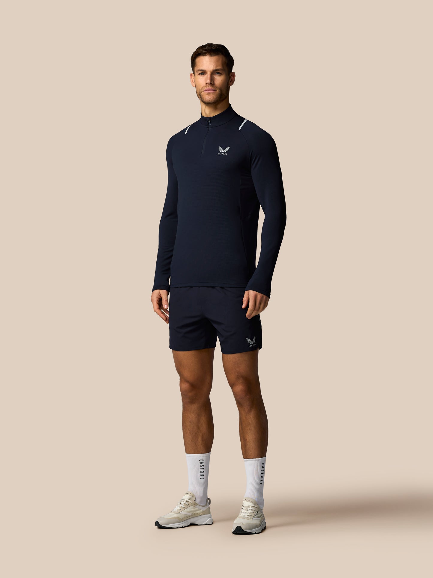 Man wearing a navy long-sleeve athletic shirt and shorts on a beige background