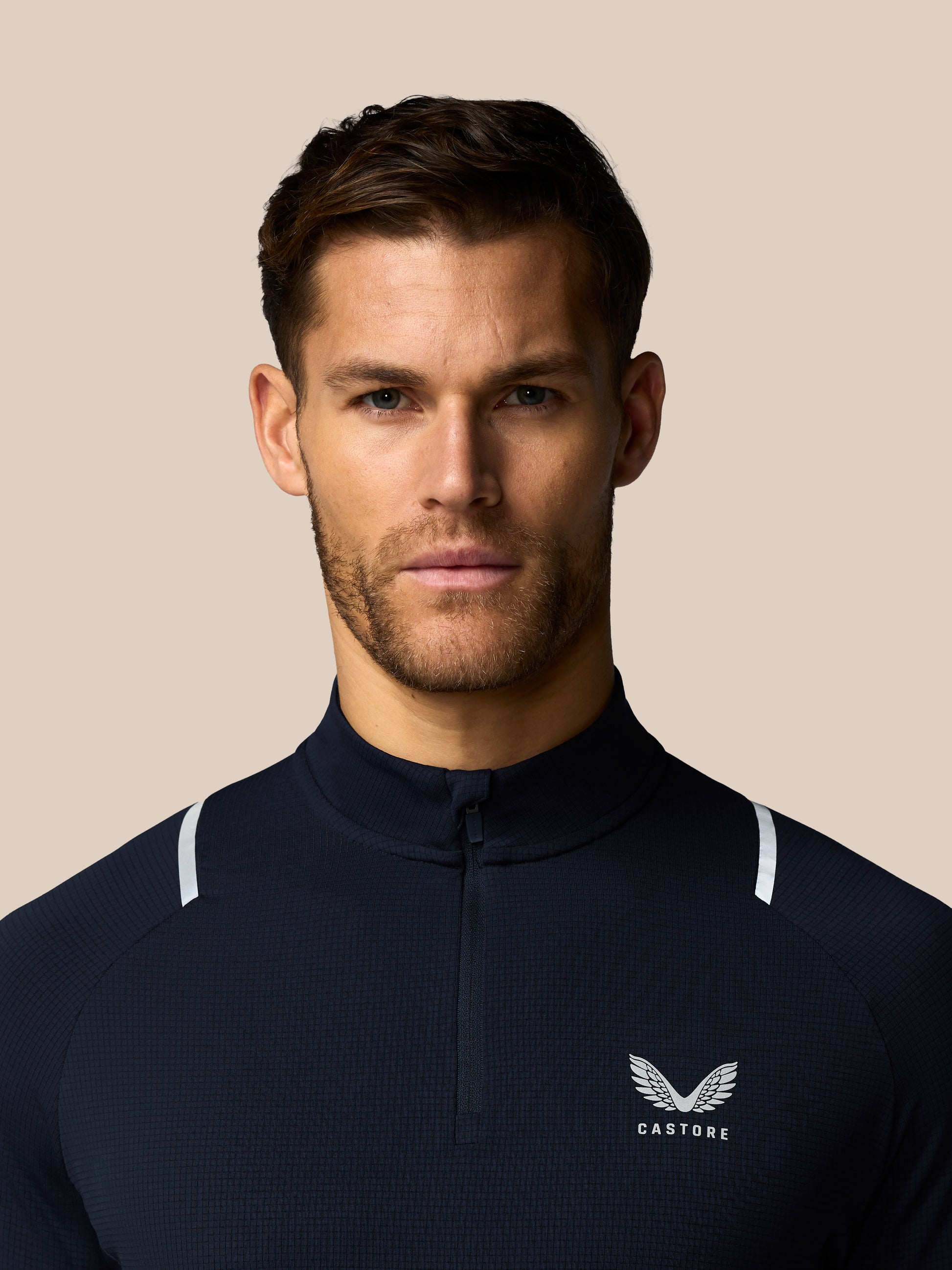 Man wearing a navy blue athletic jacket with a logo on a beige background