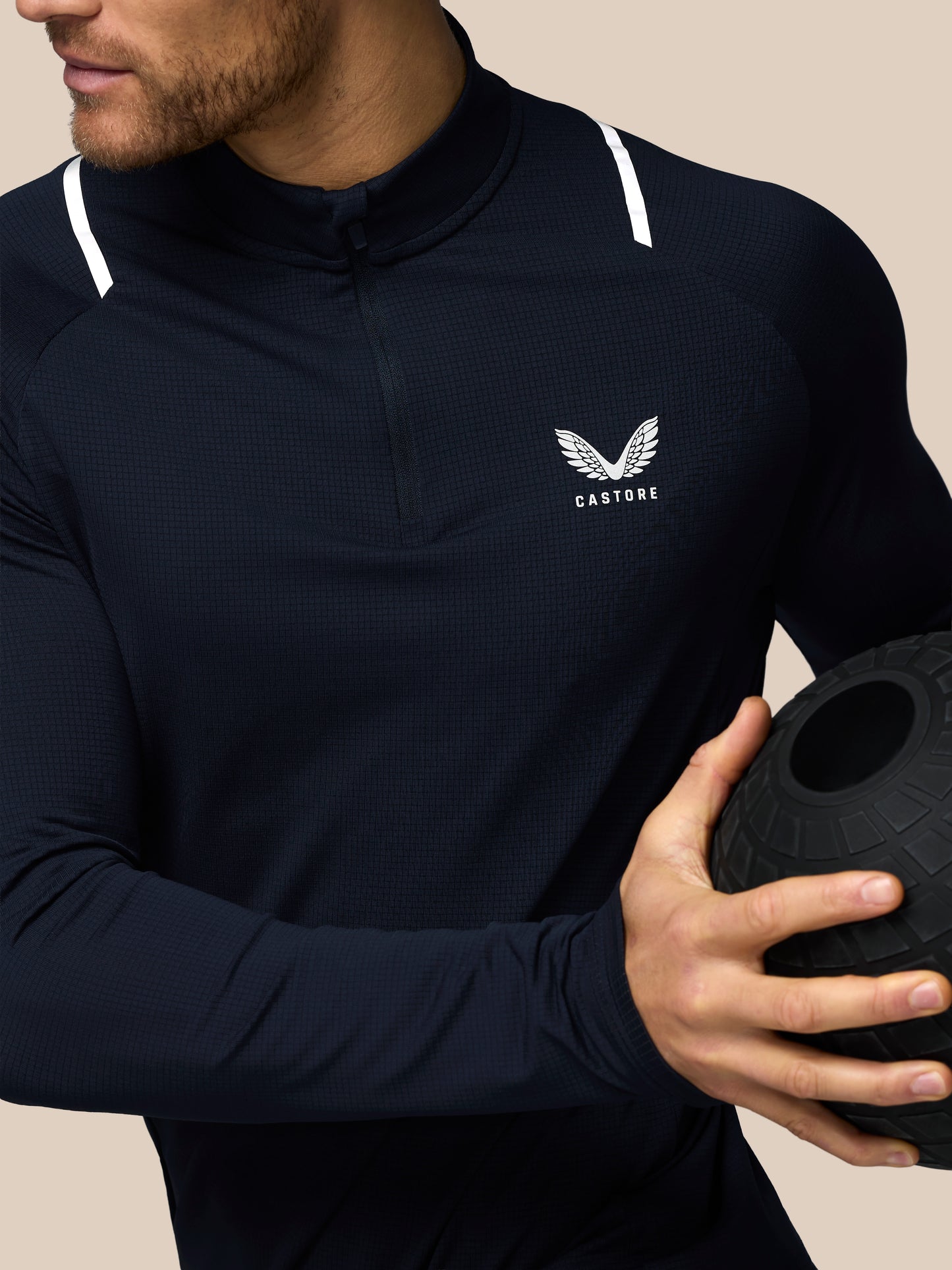 Person wearing a navy blue athletic jacket with a logo, holding a black medicine ball.