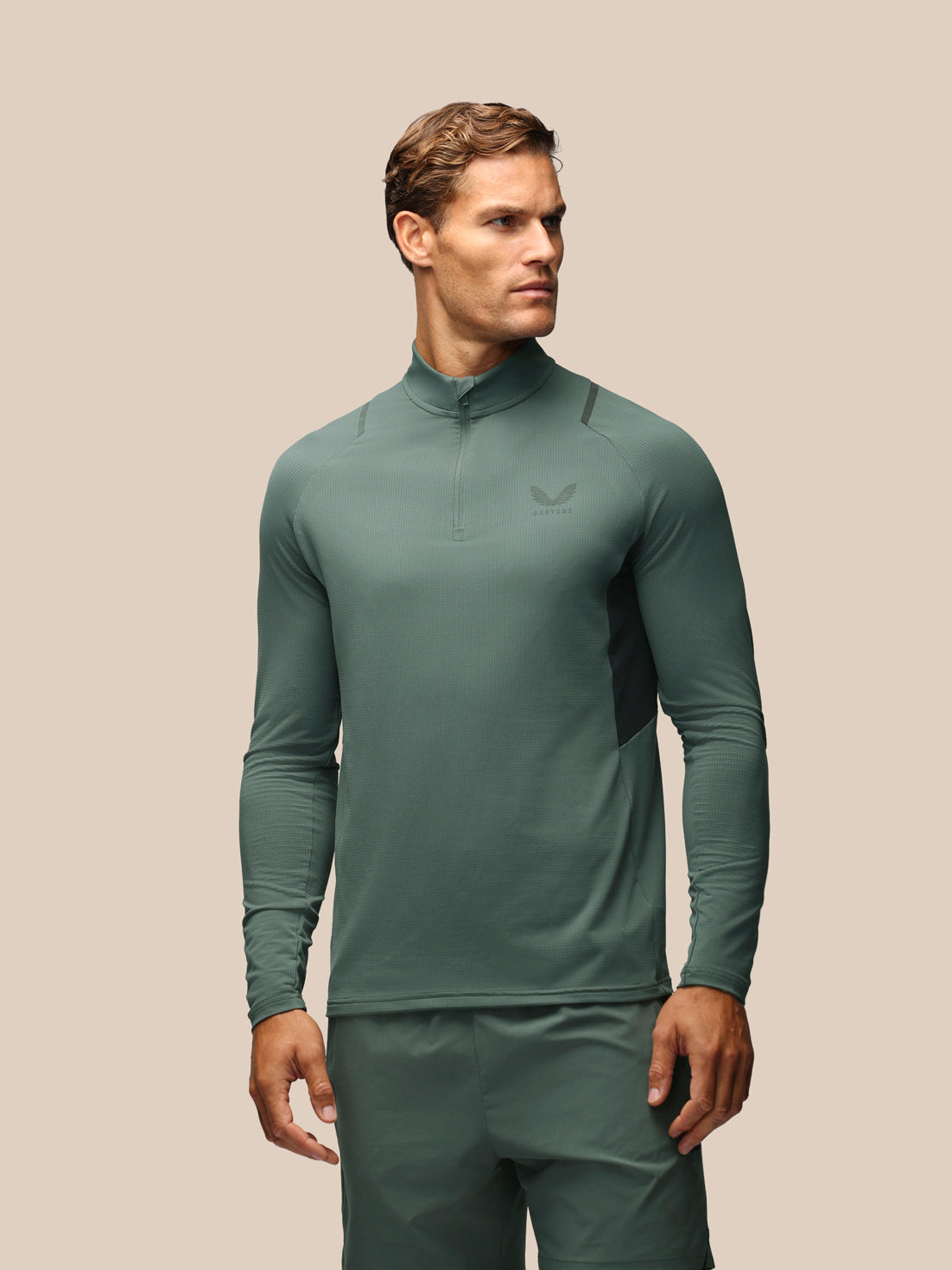A man wearing a sage green long-sleeve athletic quarter-zip pullover and matching pants, shown against a solid beige background.