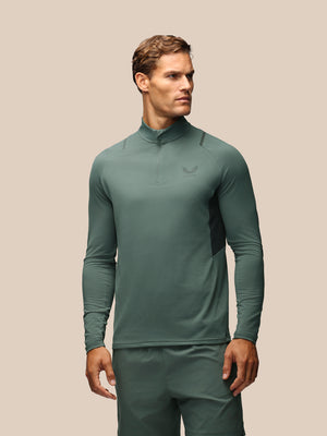 A man wearing a sage green long-sleeve athletic quarter-zip pullover and matching pants, shown against a solid beige background.