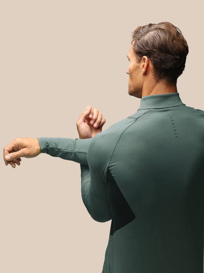 A man wearing a dark green long-sleeve athletic top, shown from the back and side against a solid beige background.