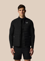 Man wearing a black puffer vest with a logo on a beige background