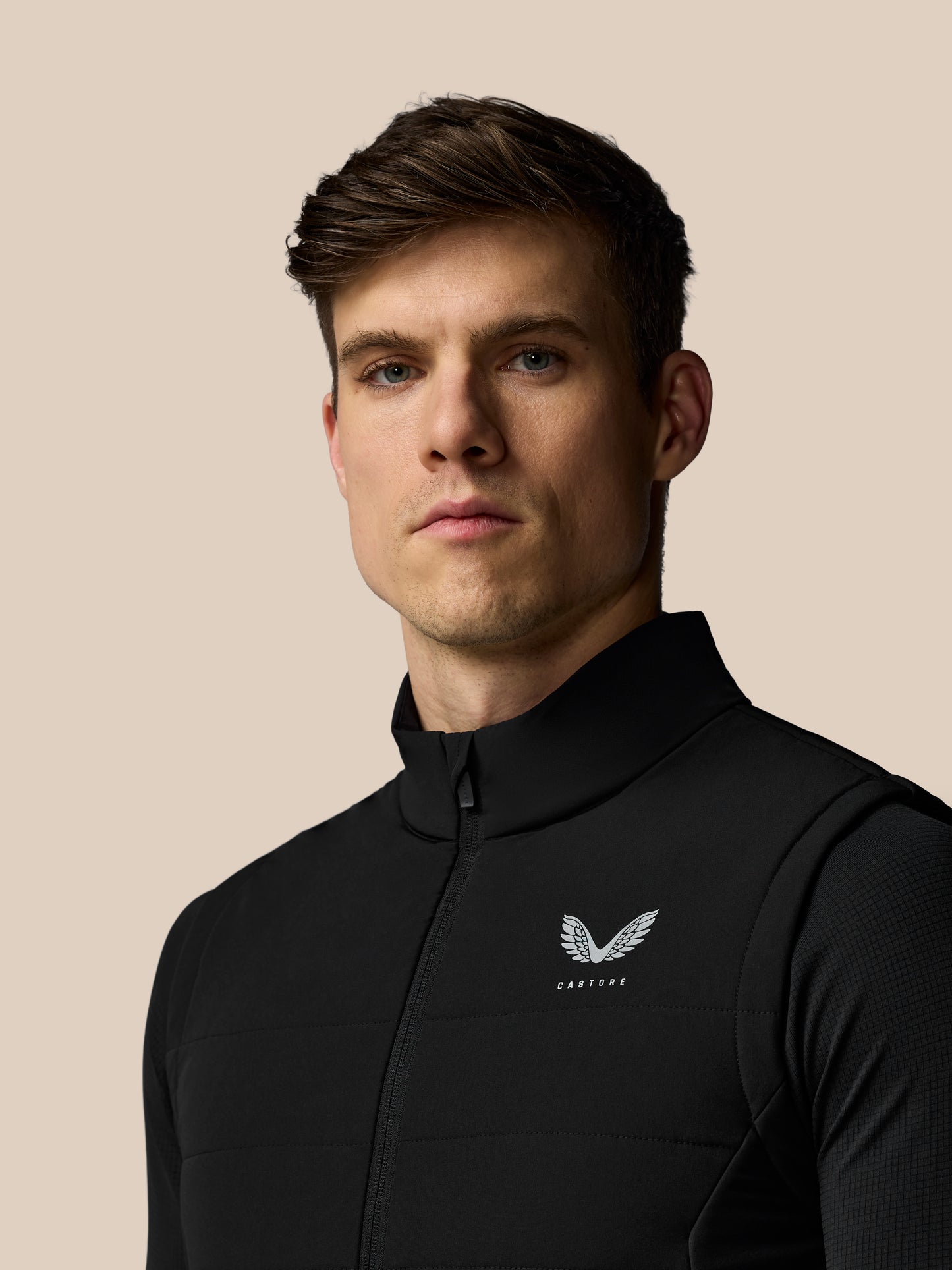 Man wearing a black jacket with a logo on a beige background