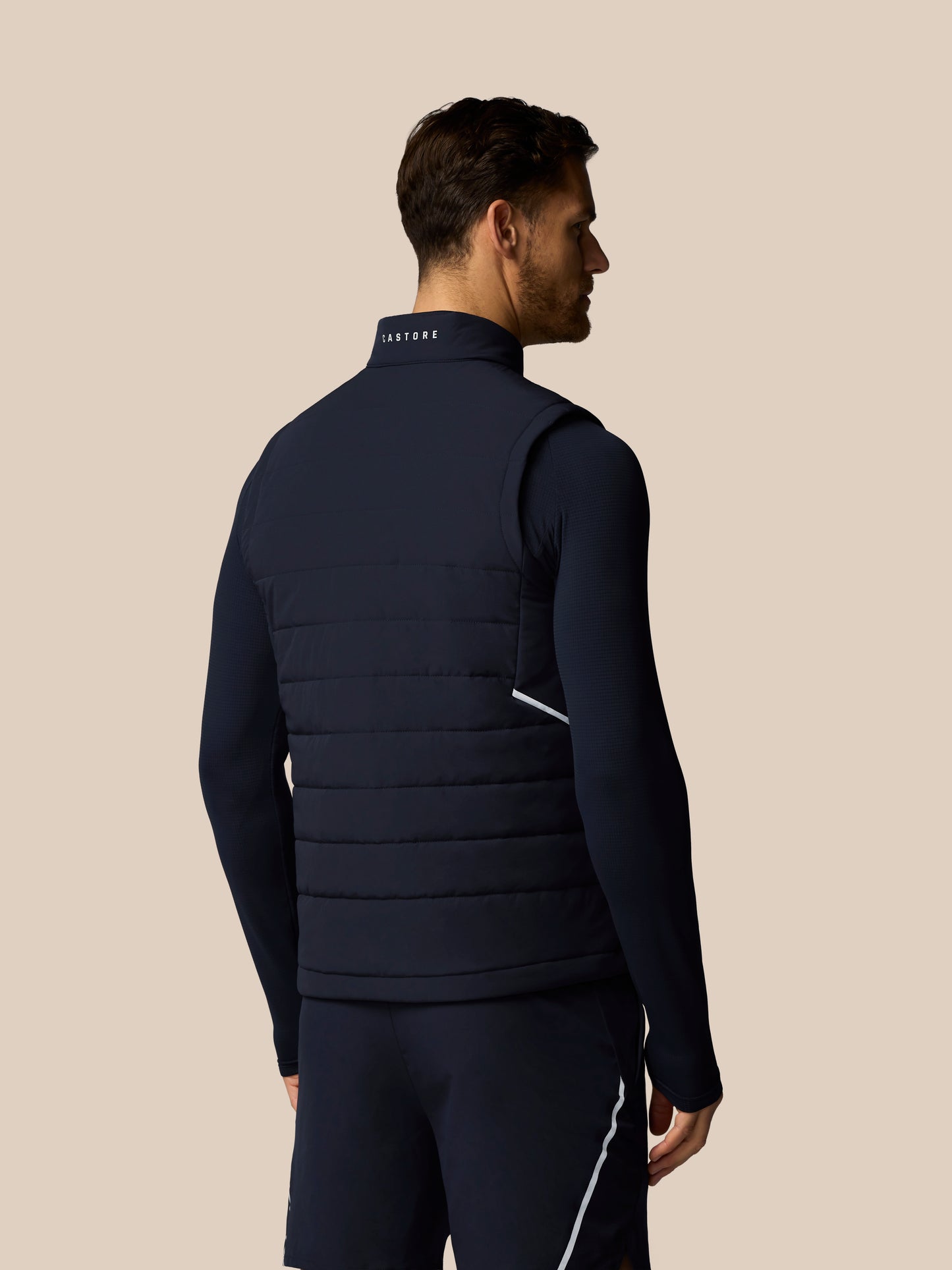 Man wearing a navy blue puffer vest on a beige background