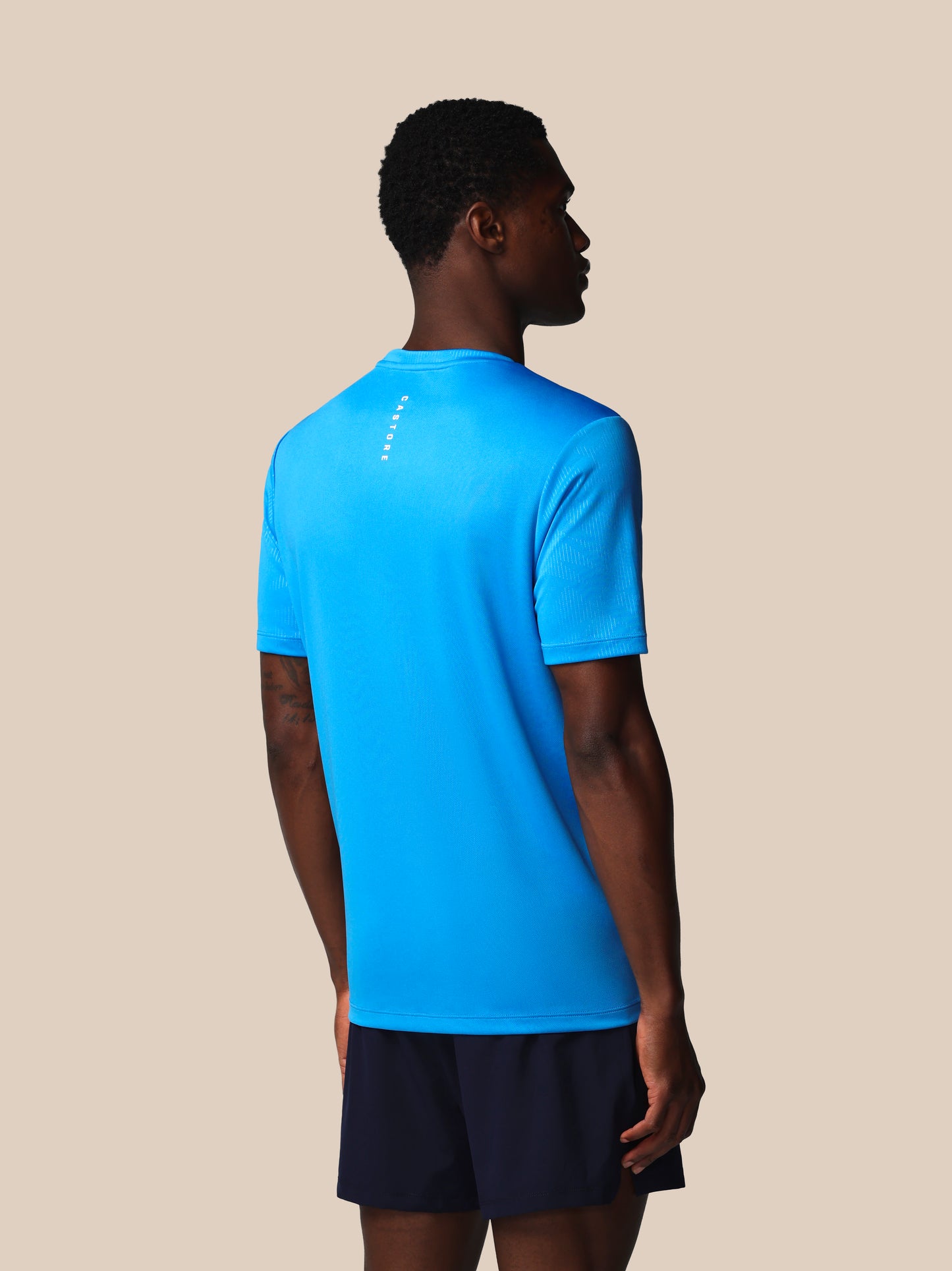 Person wearing a blue athletic shirt and black shorts on a beige background