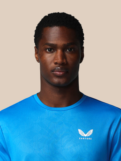 Man wearing a blue athletic shirt with a logo on a beige background