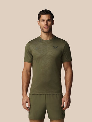 Man wearing an olive green t-shirt and shorts with a logo on a beige background