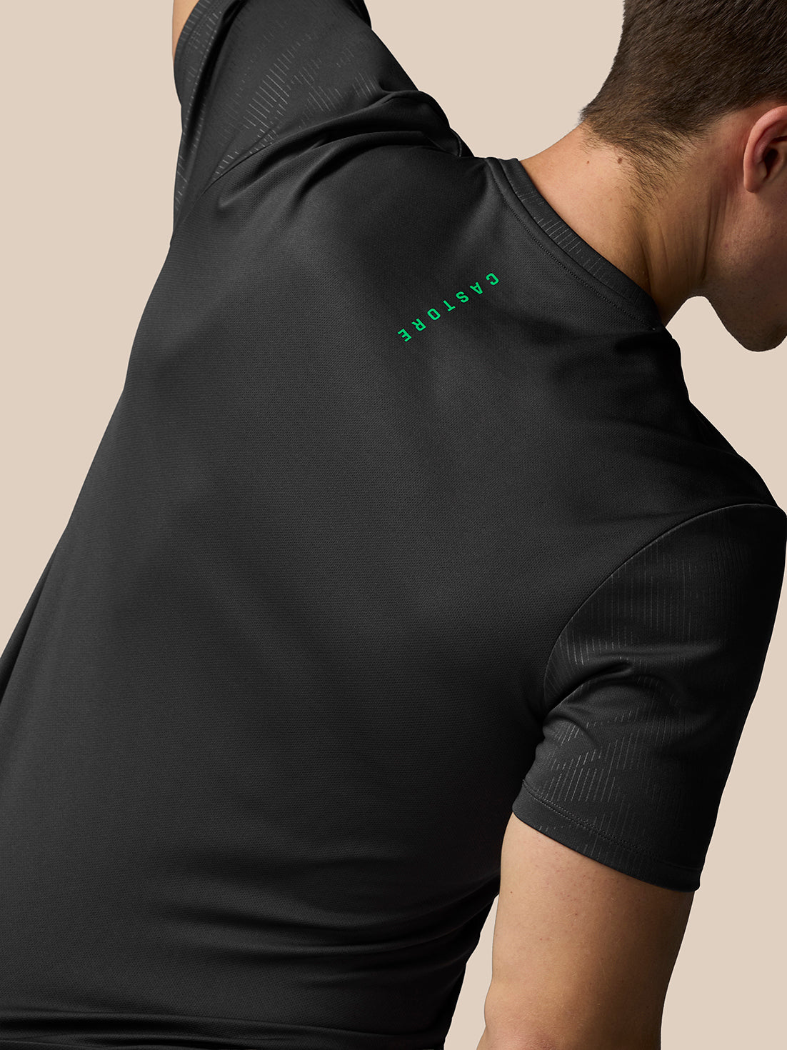 Person wearing a black athletic shirt with a green logo on a beige background