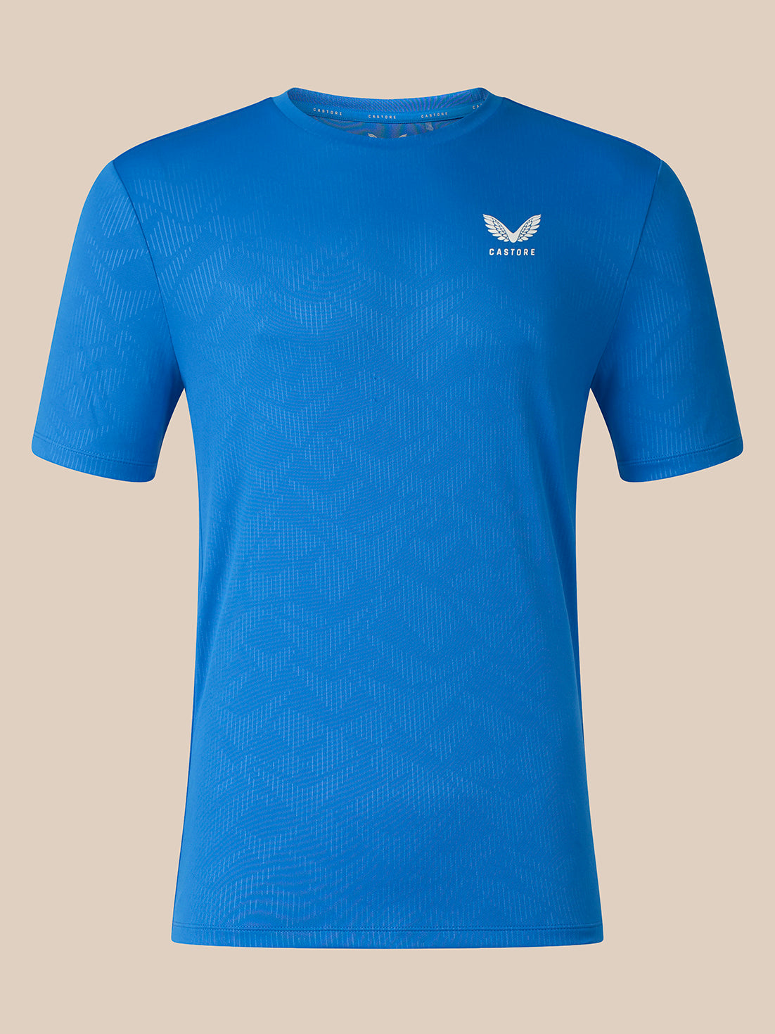 A blue short-sleeve athletic t-shirt with a subtle textured pattern and a small white winged logo on the left chest, displayed against a solid beige background.