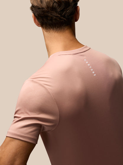A man shown from the back wearing a dusty pink short-sleeve athletic t-shirt with 'CASTORE' printed vertically in white on the upper back, set against a solid beige background.