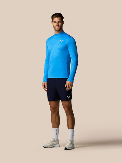 Man wearing a blue athletic long-sleeve shirt and black shorts on a beige background