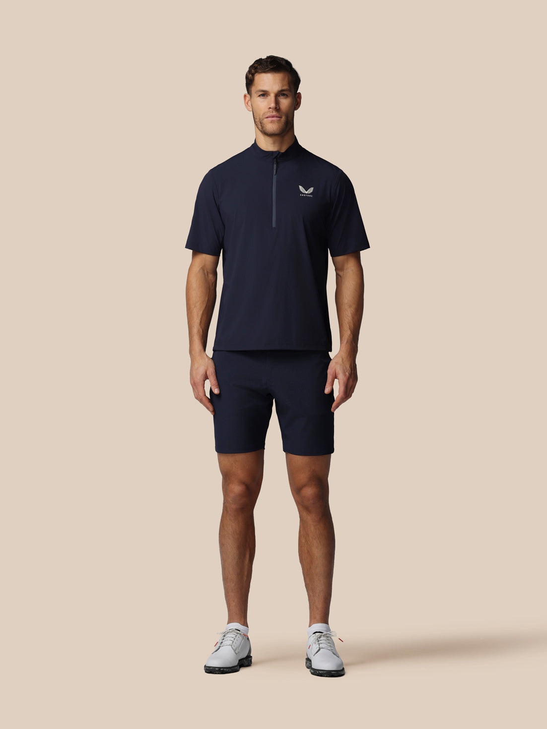 Man wearing a navy blue athletic outfit with a logo on a beige background