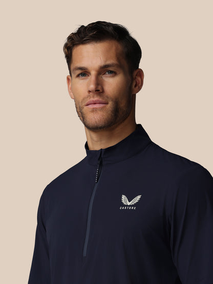 Man wearing a navy blue quarter-zip sweatshirt with Castore logo on a beige background
