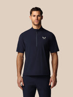 Man wearing a navy blue athletic shirt with Castore logo on a beige background