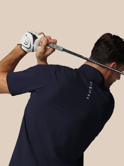 Man in navy blue shirt with 'Castore' branding holding a golf club against a beige background