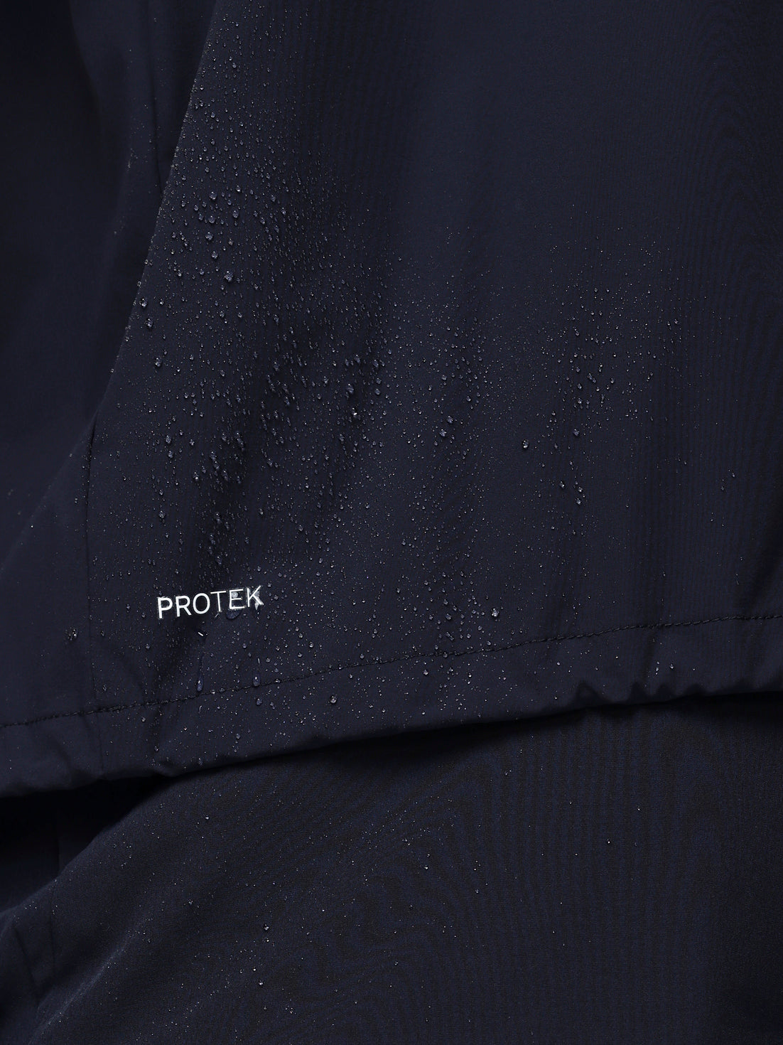 Close-up of a navy jacket with 'PROTEK' branding on a dark background