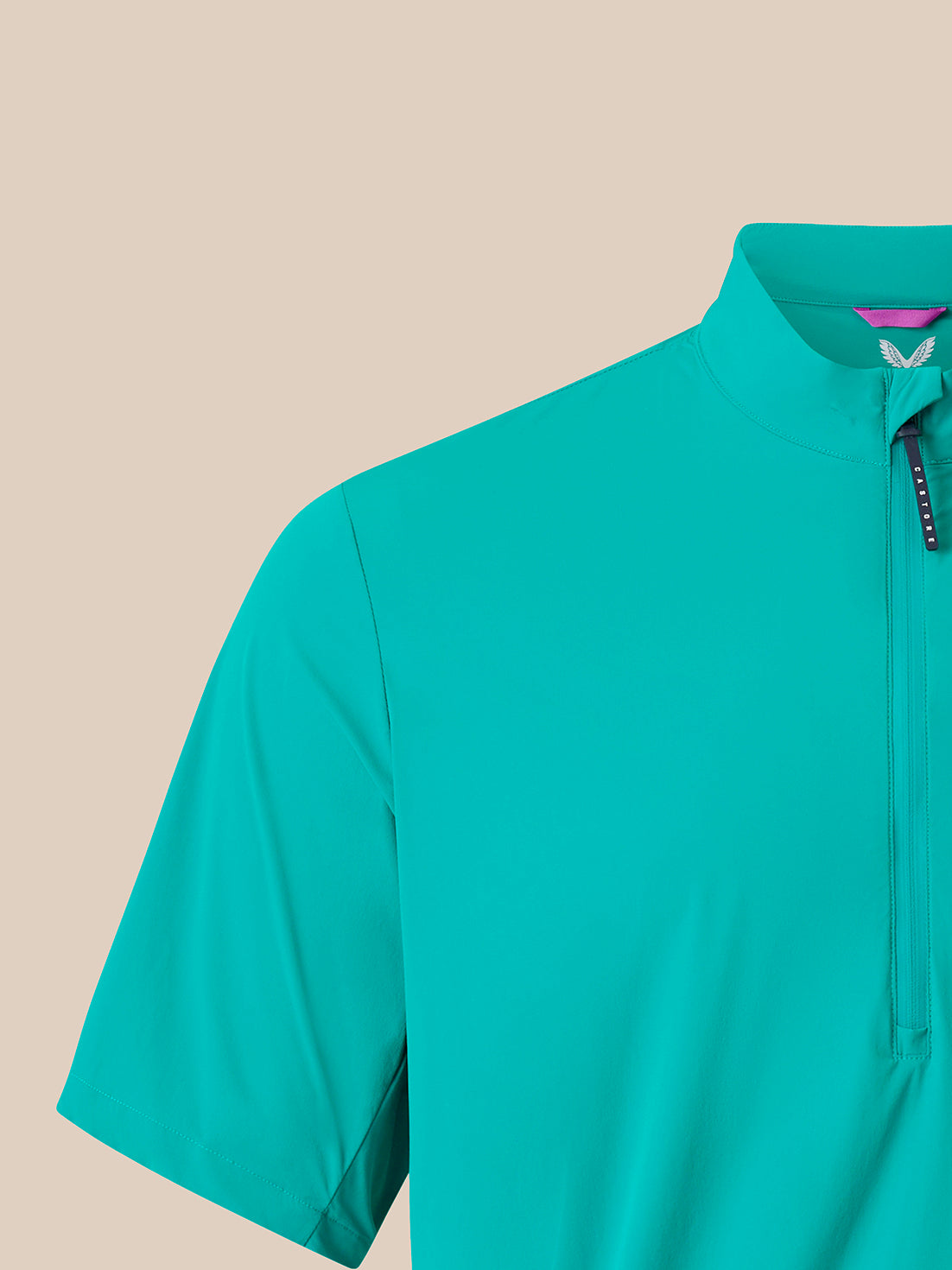 A close-up of a short-sleeve athletic half-zip pullover in a bright turquoise color, featuring a mock neck collar and a black zipper pull with white branding, set against a solid beige background.