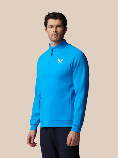 Man wearing a blue pullover with a logo on a beige background