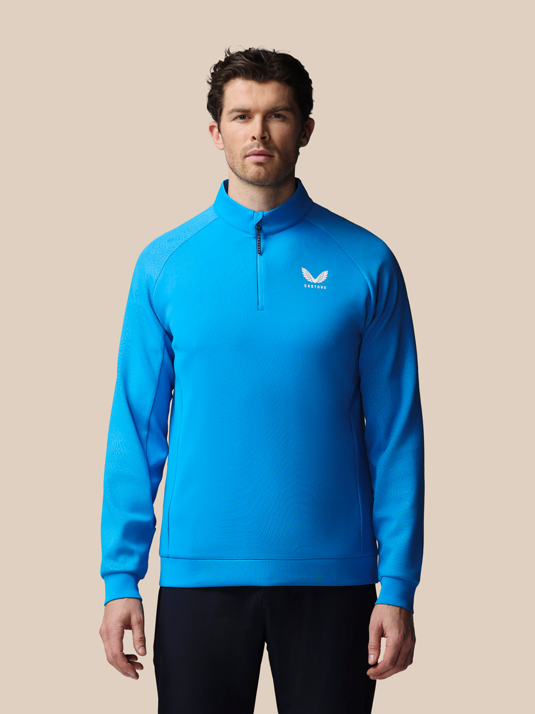 Man wearing a blue pullover with Castore logo on a beige background