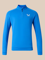 A bright blue long-sleeve quarter-zip athletic pullover with a white wing logo on the left chest, displayed on a solid beige background.