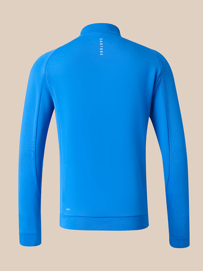 A bright blue long-sleeve quarter-zip athletic top shown from the back, featuring a small vertical white logo on the upper back and subtle textured paneling on the sleeves, set against a solid beige background.
