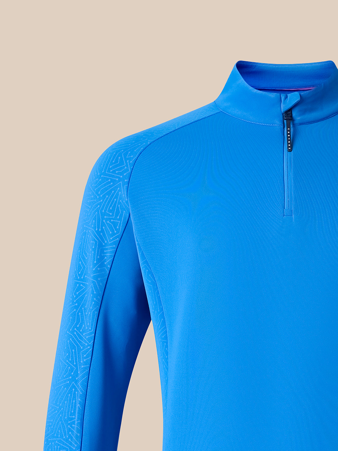 Close-up of a bright blue long-sleeve quarter-zip athletic top on a beige studio background.
